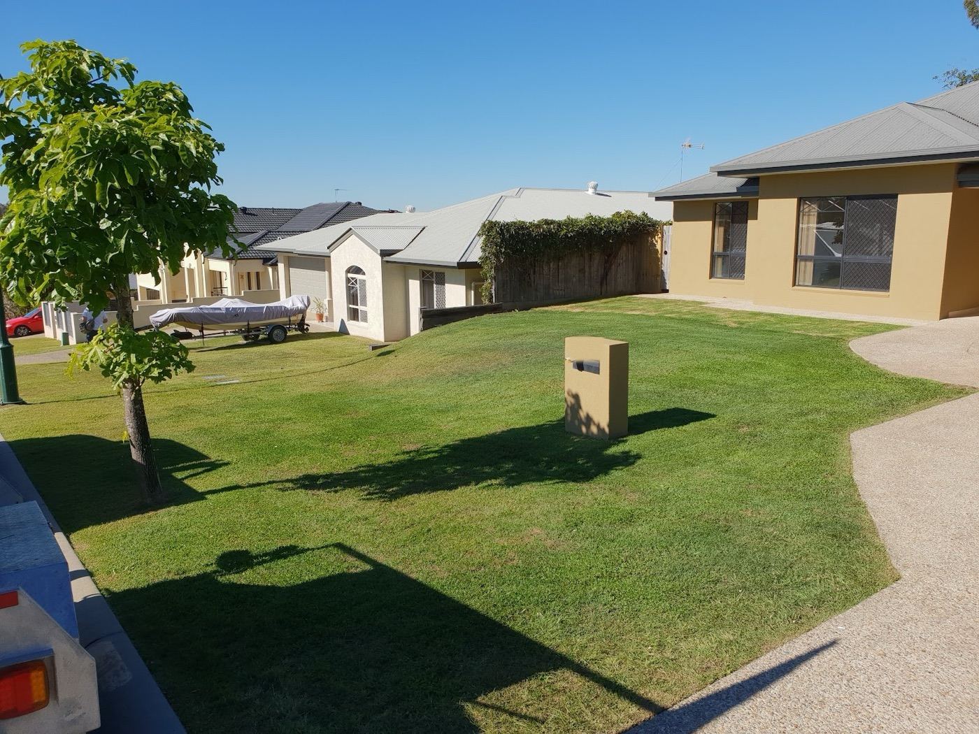 A neatly mowed front lawn sloping down to a quiet suburban street on a sunny day